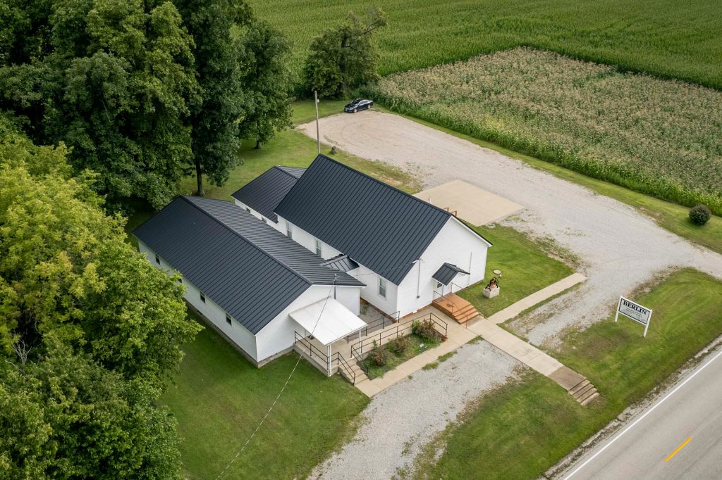 Aerial view of a church with a standing seam roof, nestled among fields and greenery.